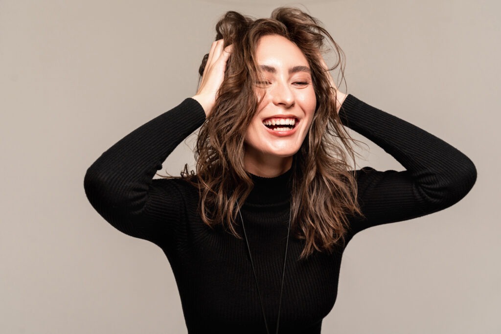 Smiling woman expressing joy with hands in hair while promoting dental health awareness